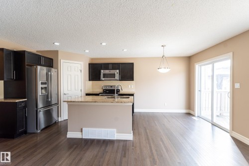 Kitchen featuring stainless steel appliances, light stone countertops, dark wood finished floors, an island with sink, and a textured ceiling - 1118 162 Street, Edmonton, AB - Indoor Photo Showing Kitchen With Stainless Steel Kitchen