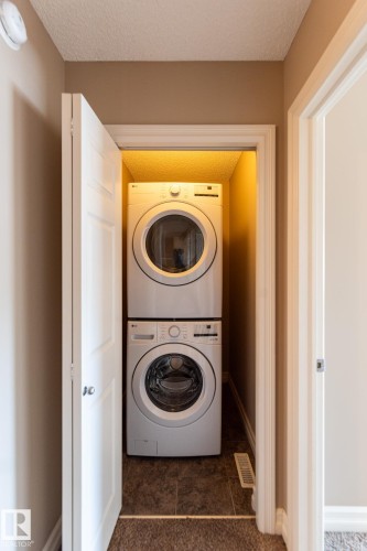 Laundry room with a textured ceiling, stacked washer / dryer, and dark tile patterned floors - 1118 162 Street, Edmonton, AB - Indoor Photo Showing Laundry Room