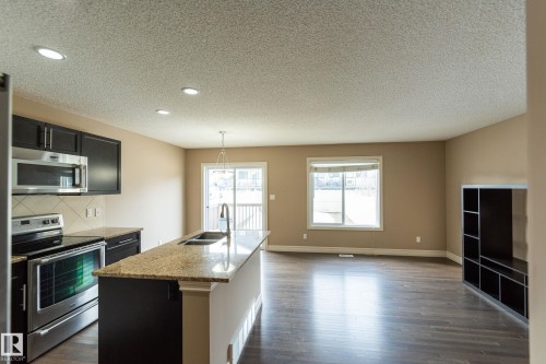 Kitchen featuring stainless steel appliances, dark cabinets, light stone counters, an island with sink, and dark wood finished floors - 1118 162 Street, Edmonton, AB - Indoor Photo Showing Kitchen With Double Sink