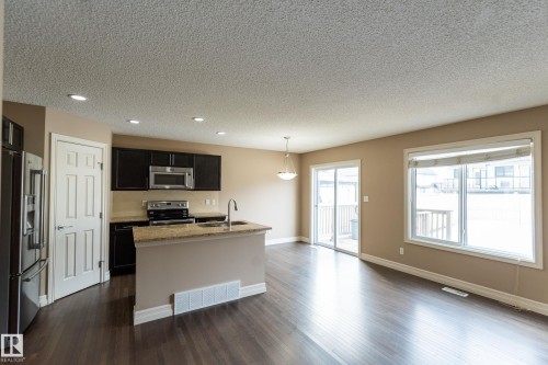 Kitchen with stainless steel appliances, a center island with sink, dark cabinets, light stone countertops, and dark wood-type flooring - 1118 162 Street, Edmonton, AB - Indoor Photo Showing Kitchen