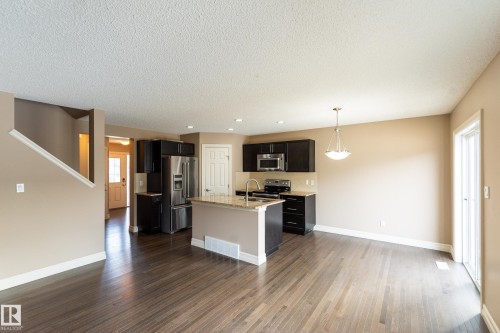 Kitchen featuring stainless steel appliances, light stone counters, dark wood-style flooring, an island with sink, and pendant lighting - 1118 162 Street, Edmonton, AB - Indoor Photo Showing Kitchen
