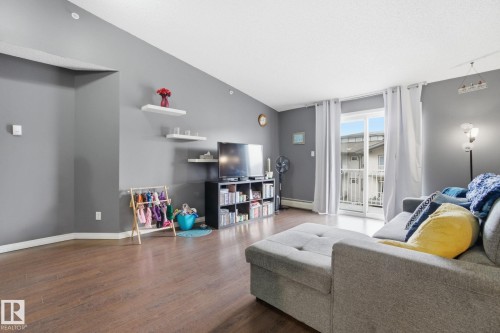 Living room with dark wood-type flooring, lofted ceiling, and a baseboard heating unit - 421 155 Edwards Drive, Edmonton, AB - Indoor Photo Showing Living Room
