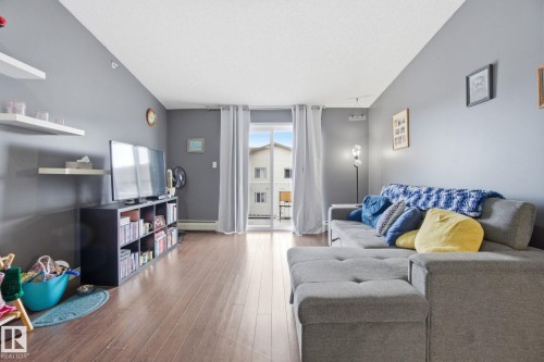 Living area with wood finished floors, a textured ceiling, and a baseboard radiator - 421 155 Edwards Drive, Edmonton, AB - Indoor Photo Showing Living Room