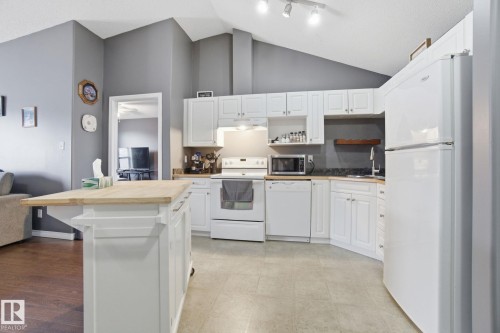 Kitchen featuring butcher block counters, white appliances, open shelves, white cabinetry, and lofted ceiling - 421 155 Edwards Drive, Edmonton, AB - Indoor Photo Showing Kitchen
