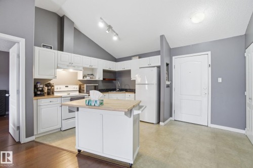Kitchen with white appliances, a kitchen island, white cabinets, butcher block counters, and lofted ceiling - 421 155 Edwards Drive, Edmonton, AB - Indoor Photo Showing Kitchen
