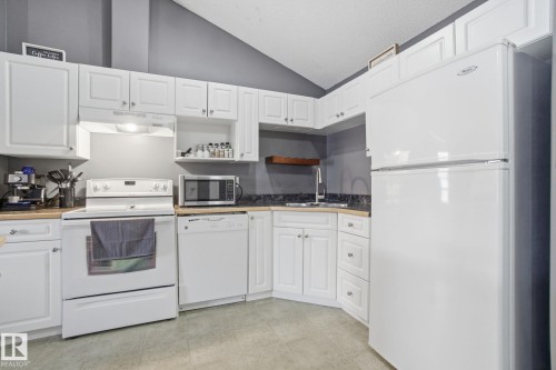 Kitchen with white appliances, lofted ceiling, open shelves, white cabinetry, and butcher block counters - 421 155 Edwards Drive, Edmonton, AB - Indoor Photo Showing Kitchen