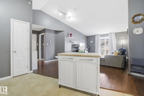Kitchen with a kitchen island, white cabinetry, open floor plan, rail lighting, and lofted ceiling - 421 155 Edwards Drive, Edmonton, AB - Indoor