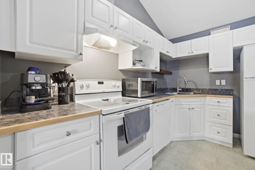 Kitchen with white appliances, white cabinets, lofted ceiling, and dark countertops - 421 155 Edwards Drive, Edmonton, AB - Indoor Photo Showing Kitchen