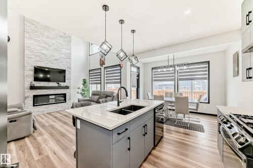 Kitchen featuring a kitchen island with sink, light wood-style flooring, a fireplace, gray cabinets, and a high ceiling - 5110 23A Avenue, Edmonton, AB - Indoor Photo Showing Kitchen With Double Sink With Upgraded Kitchen