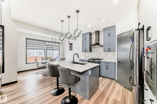Kitchen featuring a center island with sink, a breakfast bar, light wood-style floors, gray cabinetry, and backsplash - 5110 23A Avenue, Edmonton, AB - Indoor Photo Showing Kitchen With Upgraded Kitchen