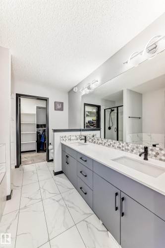 Full bath with a walk in closet, a stall shower, double vanity, light marble finish flooring, and a textured ceiling - 5110 23A Avenue, Edmonton, AB - Indoor Photo Showing Bathroom