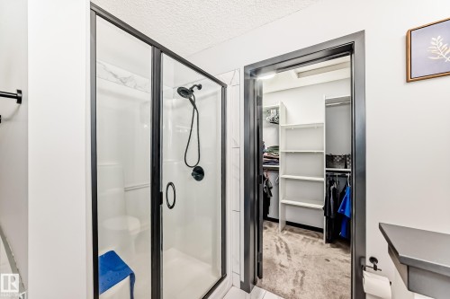 Bathroom with a textured ceiling, a stall shower, a spacious closet, and light colored carpet - 5110 23A Avenue, Edmonton, AB - Indoor Photo Showing Bathroom
