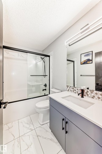 Bathroom featuring combined bath / shower with glass door, vanity, a textured ceiling, and light marble finish flooring - 5110 23A Avenue, Edmonton, AB - Indoor Photo Showing Bathroom
