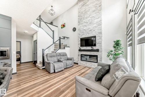 Living room featuring a stone fireplace, light wood finished floors, and a high ceiling - 5110 23A Avenue, Edmonton, AB - Indoor Photo Showing Living Room With Fireplace