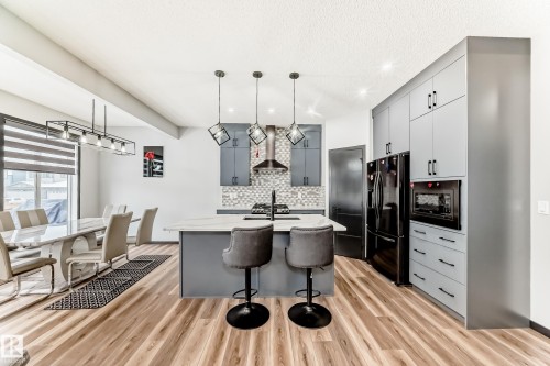 Kitchen with decorative light fixtures, an island with sink, gray cabinetry, and black appliances - 5110 23A Avenue, Edmonton, AB - Indoor
