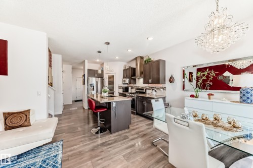 Kitchen featuring a breakfast bar area, dark wood finish cabinetry, an island with sink, stainless steel appliances, and light wood finished floors - 3059 Checknita Way, Edmonton, AB - Indoor