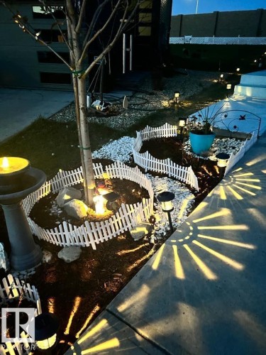 The property features decorative outdoor lighting, a birdbath, and landscaped garden beds with white picket fencing - 3059 Checknita Way, Edmonton, AB - Outdoor
