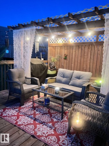The outdoor deck features a wooden pergola with string lights, a privacy screen, and a solid wooden fence - 3059 Checknita Way, Edmonton, AB - Outdoor With Deck Patio Veranda