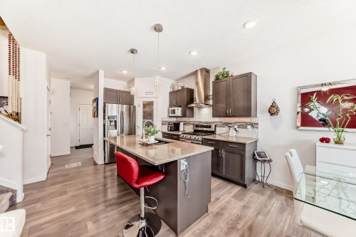 Kitchen featuring ventilation hood, dark wood finish cabinetry, a center island with sink, a breakfast bar area, and light stone counters - 3059 Checknita Way, Edmonton, AB - Indoor Photo Showing Kitchen With Double Sink With Upgraded Kitchen