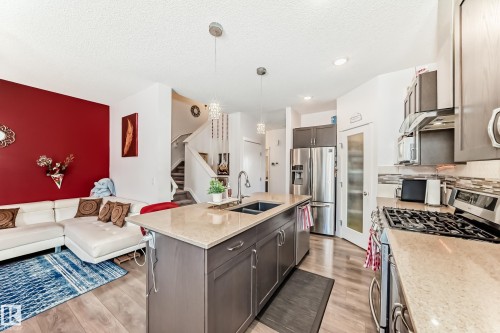 Kitchen with stainless steel appliances, light stone counters, open floor plan, dark wood finish cabinetry, and decorative light fixtures - 3059 Checknita Way, Edmonton, AB - Indoor Photo Showing Kitchen With Double Sink With Upgraded Kitchen