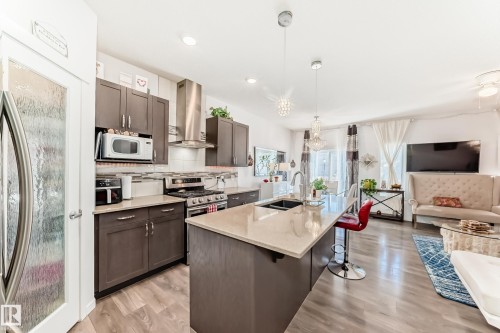 Kitchen with open floor plan, dark wood finish cabinets, range hood, a center island with sink, and light wood finished floors - 3059 Checknita Way, Edmonton, AB - Indoor Photo Showing Kitchen With Double Sink With Upgraded Kitchen
