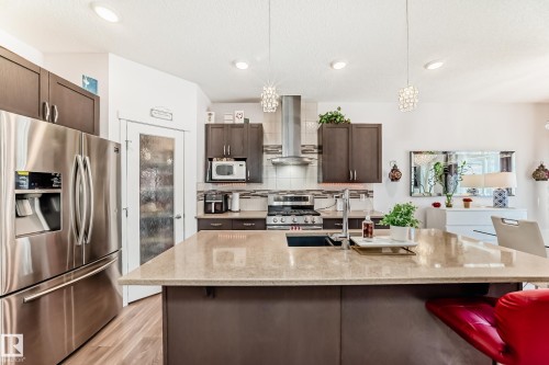 Kitchen with stainless steel appliances, dark wood finish cabinetry, light stone counters, a kitchen bar, and a textured ceiling - 3059 Checknita Way, Edmonton, AB - Indoor Photo Showing Kitchen With Upgraded Kitchen