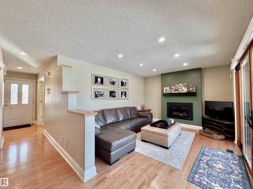Family room with light wood-style floors, a textured ceiling, a glass covered fireplace, and recessed lighting - 4 Wolf Crescent Nw, Edmonton, AB - Indoor Photo Showing Living Room With Fireplace