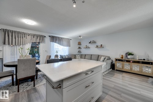 Kitchen featuring a center island, light stone counters, open floor plan, a textured ceiling, and light wood-style floors - 59 14803 Miller Boulevard, Edmonton, AB - Indoor
