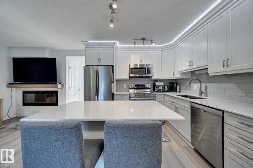 Kitchen featuring a kitchen island, stainless steel appliances, light stone counters, light wood-style floors, and a textured ceiling - 59 14803 Miller Boulevard, Edmonton, AB - Indoor Photo Showing Kitchen With Double Sink With Upgraded Kitchen