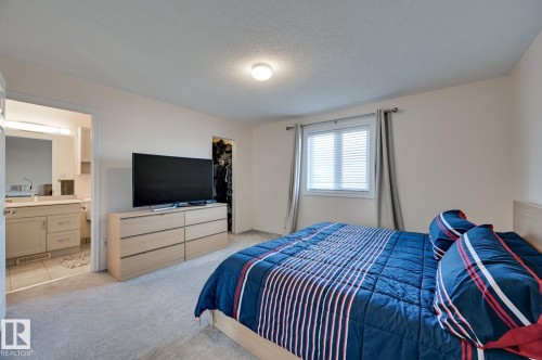 Bedroom with light carpet, a textured ceiling, a spacious closet, and connected bathroom - 59 14803 Miller Boulevard, Edmonton, AB - Indoor Photo Showing Bedroom