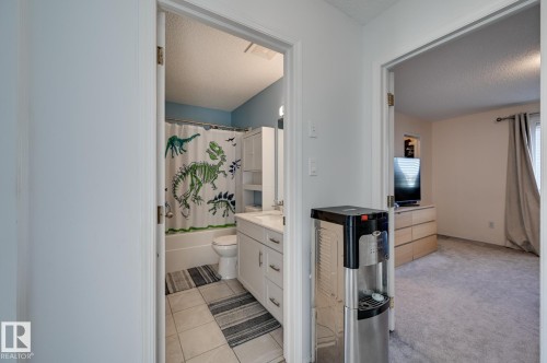 Full bath with vanity, shower / bath combo, a textured ceiling, light tile patterned flooring, and light colored carpet - 59 14803 Miller Boulevard, Edmonton, AB - Indoor