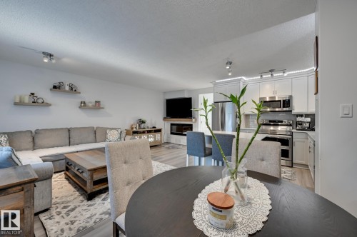 Dining area with a textured ceiling, light wood finished floors, track lighting, and a glass covered fireplace - 59 14803 Miller Boulevard, Edmonton, AB - Indoor