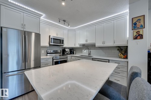 Kitchen with stainless steel appliances, white cabinets, a kitchen island, a textured ceiling, and decorative backsplash - 59 14803 Miller Boulevard, Edmonton, AB - Indoor Photo Showing Kitchen With Upgraded Kitchen