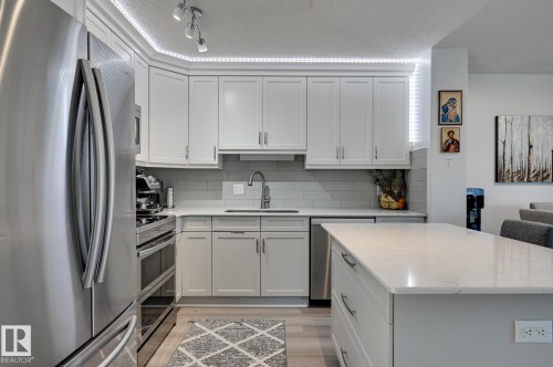 Kitchen featuring stainless steel appliances, light stone countertops, light wood-type flooring, decorative backsplash, and white cabinetry - 59 14803 Miller Boulevard, Edmonton, AB - Indoor Photo Showing Kitchen With Upgraded Kitchen
