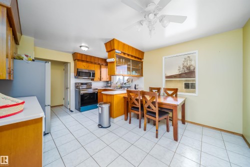 The kitchen features tile flooring, wood cabinetry, a stainless steel microwave, and a window providing natural light - 7911 145 Avenue Nw, Edmonton, AB - Indoor