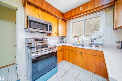 Kitchen featuring wooden cabinetry, white countertops, tile flooring, a double basin sink, and a stainless steel oven with an overhead microwave - 7911 145 Avenue Nw, Edmonton, AB - Indoor Photo Showing Kitchen With Double Sink