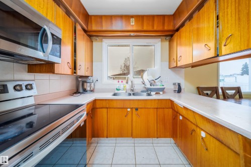 The kitchen features wood cabinetry, white countertops, and a stainless steel over-the-range microwave - 7911 145 Avenue Nw, Edmonton, AB - Indoor Photo Showing Kitchen With Double Sink