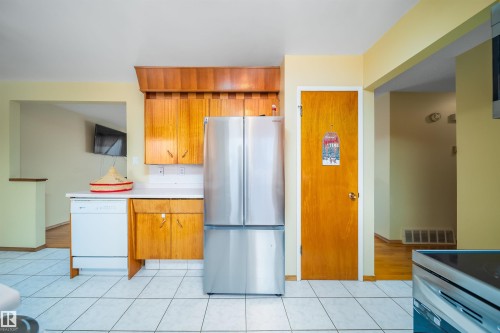 The kitchen features wood cabinetry, white countertops, a stainless steel refrigerator, and a white tile floor - 7911 145 Avenue Nw, Edmonton, AB - Indoor Photo Showing Kitchen