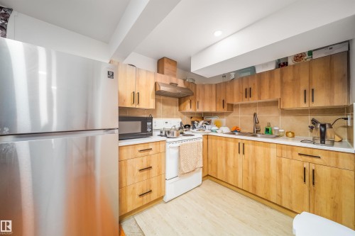 The kitchen features light wood cabinetry, a stainless steel refrigerator, and a light-colored tiled backsplash - 7911 145 Avenue Nw, Edmonton, AB - Indoor Photo Showing Kitchen