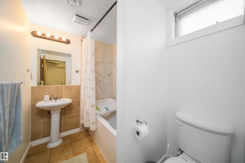The bathroom features a pedestal sink, a tiled vanity backsplash, a bathtub with tiled surround, and a toilet - 7911 145 Avenue Nw, Edmonton, AB - Indoor Photo Showing Bathroom