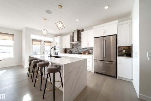 Kitchen featuring stainless steel appliances, white cabinetry, a breakfast bar, light wood finished floors, and a textured ceiling - 19 Sturtz Place, Leduc, AB - Indoor Photo Showing Kitchen With Upgraded Kitchen