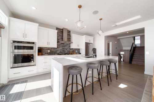 Kitchen featuring pendant lighting, a kitchen breakfast bar, a center island with sink, white cabinets, and backsplash - 19 Sturtz Place, Leduc, AB - Indoor Photo Showing Kitchen With Upgraded Kitchen
