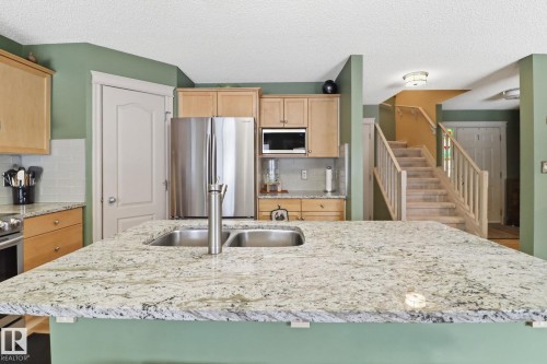 Kitchen with light wood finish cabinets, stainless steel appliances, light stone countertops, a center island with sink, and a textured ceiling - 8311 11 Avenue, Edmonton, AB - Indoor Photo Showing Kitchen With Stainless Steel Kitchen With Double Sink With Upgraded Kitchen