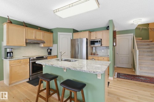 Kitchen with light wood finish cabinets, light stone countertops, stainless steel appliances, a kitchen bar, and a textured ceiling - 8311 11 Avenue, Edmonton, AB - Indoor Photo Showing Kitchen With Stainless Steel Kitchen With Double Sink With Upgraded Kitchen