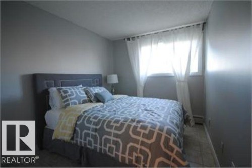 This room features neutral gray walls, a window with sheer white curtains, and tile flooring - 12 11265 31 Avenue, Edmonton, AB - Indoor Photo Showing Bedroom