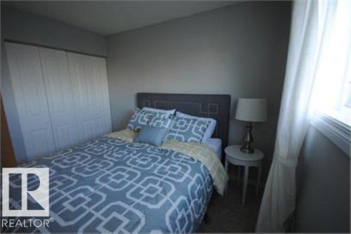 The room features a bed with a headboard, a window with curtains, and a nightstand with a lamp - 12 11265 31 Avenue, Edmonton, AB - Indoor Photo Showing Bedroom