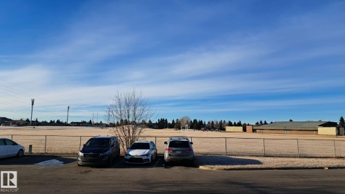View of an expansive outdoor area with a fence, trees, and a distant building visible under a clear sky - 12 11265 31 Avenue, Edmonton, AB - Outdoor With View