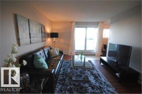 Living area featuring hardwood flooring, a large window with white curtains, and a dark area rug - 12 11265 31 Avenue, Edmonton, AB - Indoor Photo Showing Living Room