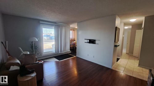 Living area with hardwood flooring, a large window providing natural light, and a tiled entryway - 12 11265 31 Avenue, Edmonton, AB - Indoor