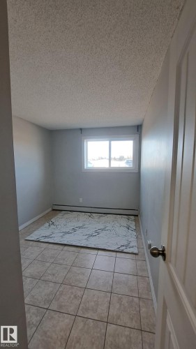 This room features neutral-toned tiled flooring, a window providing natural light, and light-colored walls - 12 11265 31 Avenue, Edmonton, AB - Indoor Photo Showing Other Room